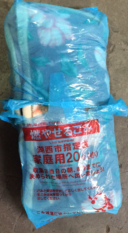 可燃ごみ用ごみ袋2枚をもって納まる様試みられているものの袋の口が縛られていない毛布の廃棄物の写真