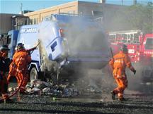 ゴミ収集車の火災(スプレー缶やカセットボンベの引火)を消防士が消している写真