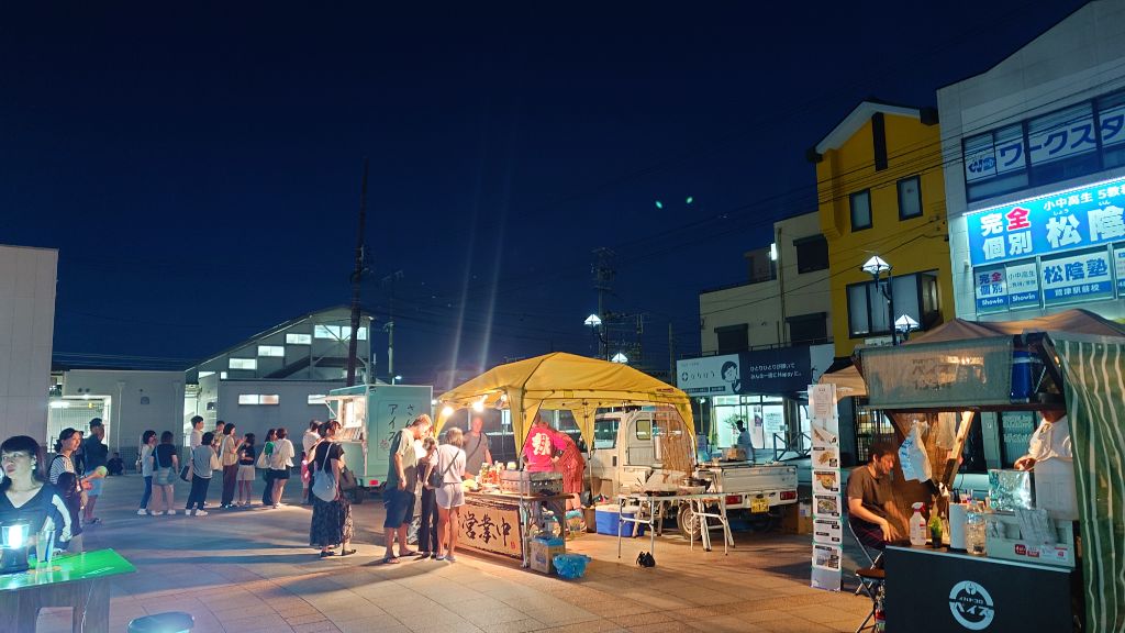 2025年に開催したちょこっと夜市の様子。夜の駅前に屋台やテントが並び、人々が並んだり飲食したりしている。